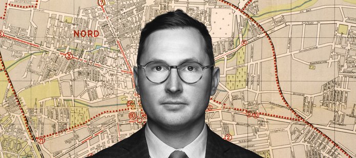 Dr Adam Sitarek na tle fragmentu mapy łódzkiego getta