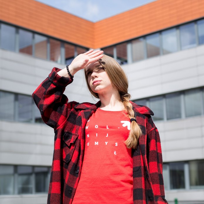 Dziewczyna patrzy w stronę słońca i osłania oczy, w tle budynek WZ