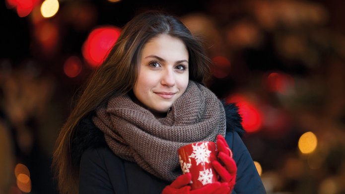 a smiling woman with dark long hair holding a red mug decorated with white snowflakes