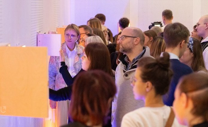 A group of people at the exhibition looking into boxes hanging on the wall.