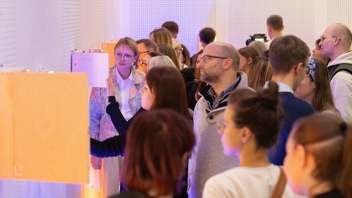 A group of people at the exhibition looking into boxes hanging on the wall.