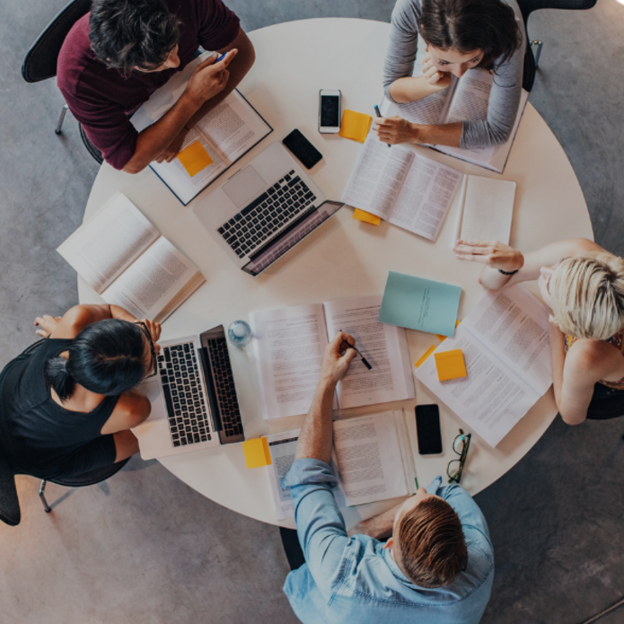 grupa ludzi pracujących przy okrągłym stole z notesami i komputerami 