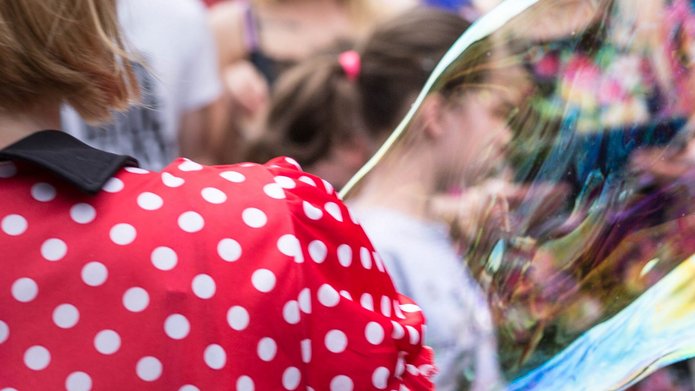 A woman wearing a red dress with white polka dots with soap bubbles, other people visible in the background