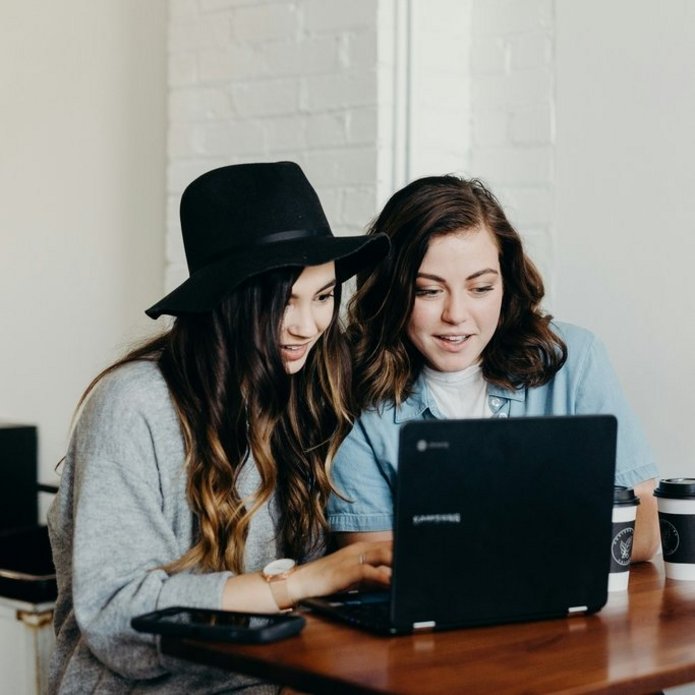 Zdjęcie poglądowe. Dwie uśmiechnięte dziewczyny wpatrzone w ekran laptopa.