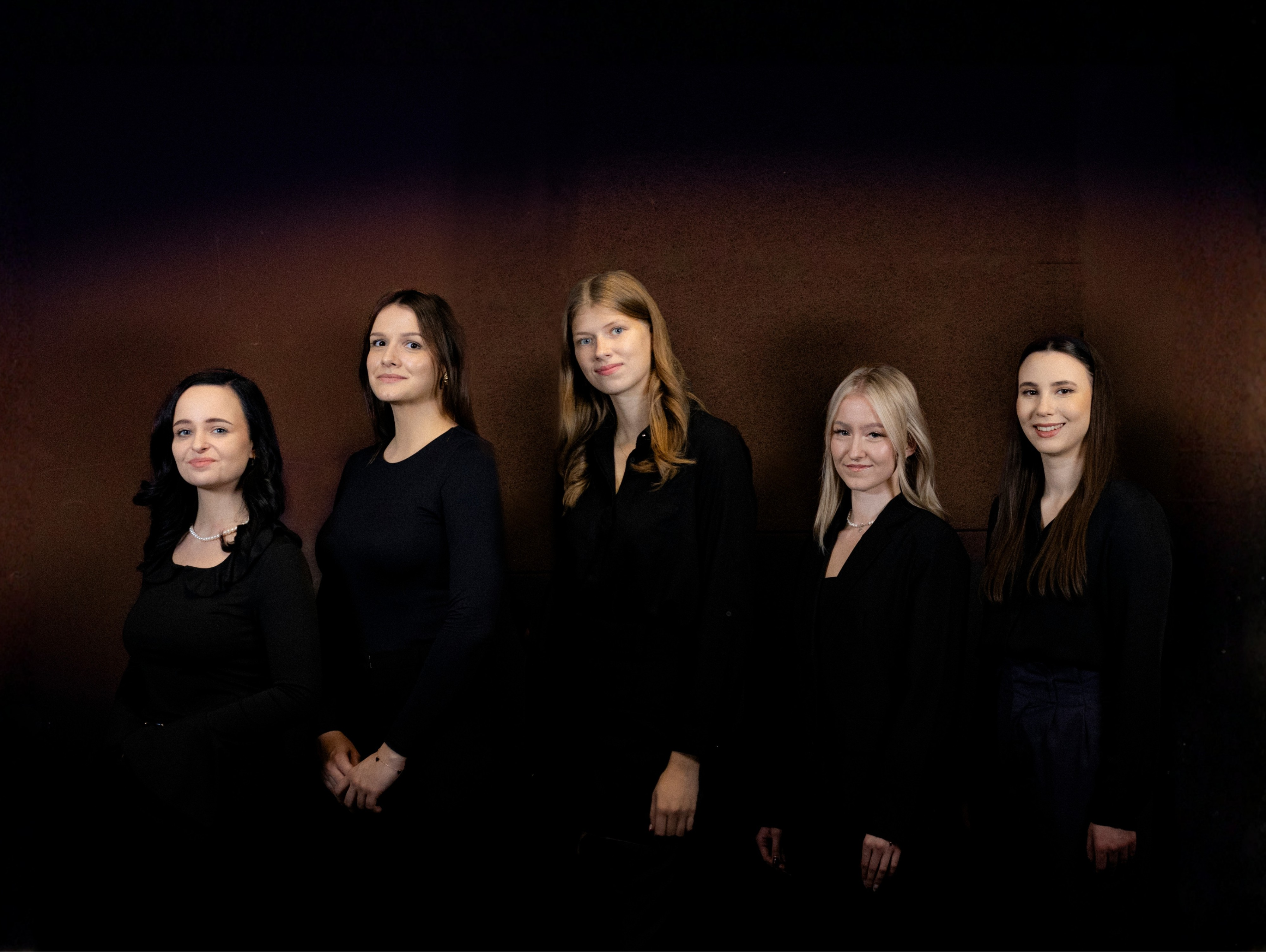 Pięć dziewczyn ubranych na czarno stojących na ciemnym tle