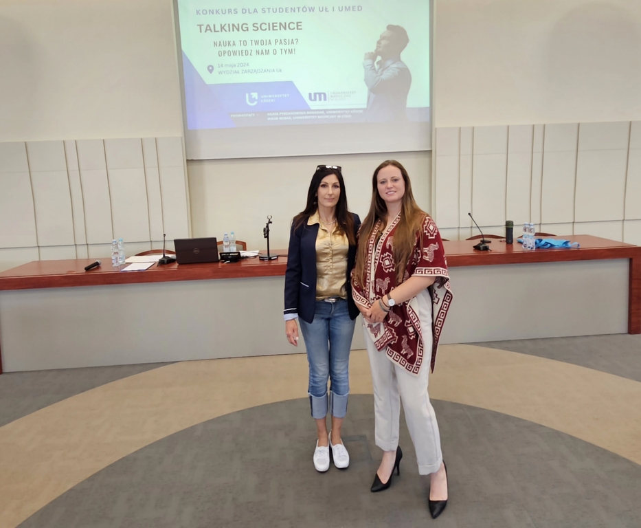 Karina Woźniak z dr Beatą Borowską stoją na tle wyświetlonego plakatu konkursu Talking Science w sali wykładowej