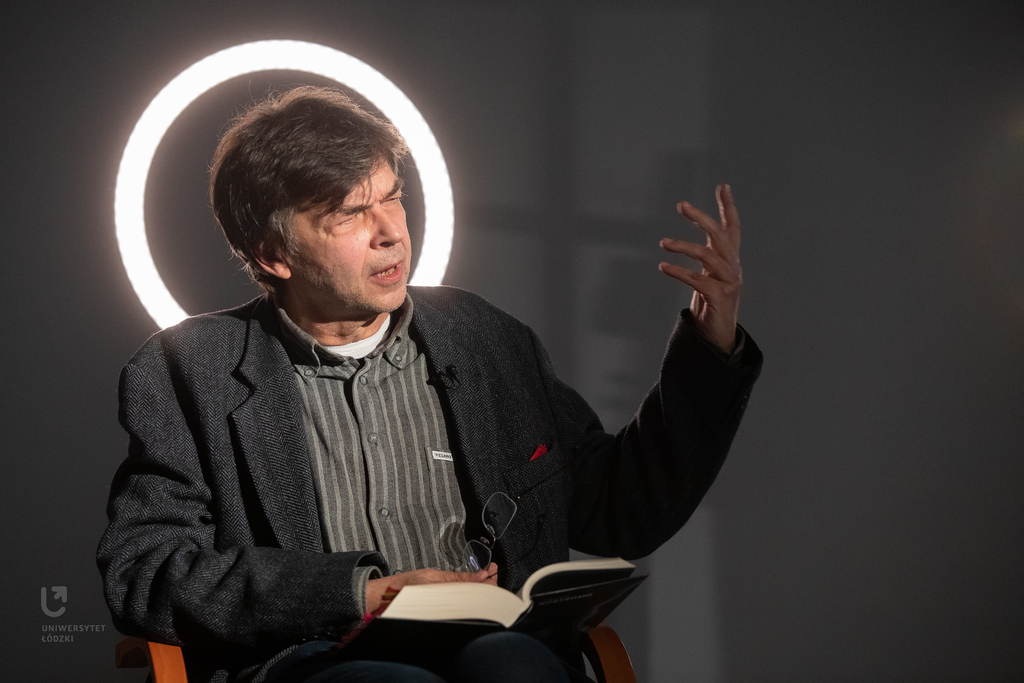 Autor tłumaczenia siedzi w sali i opowiada, gestykulując. 