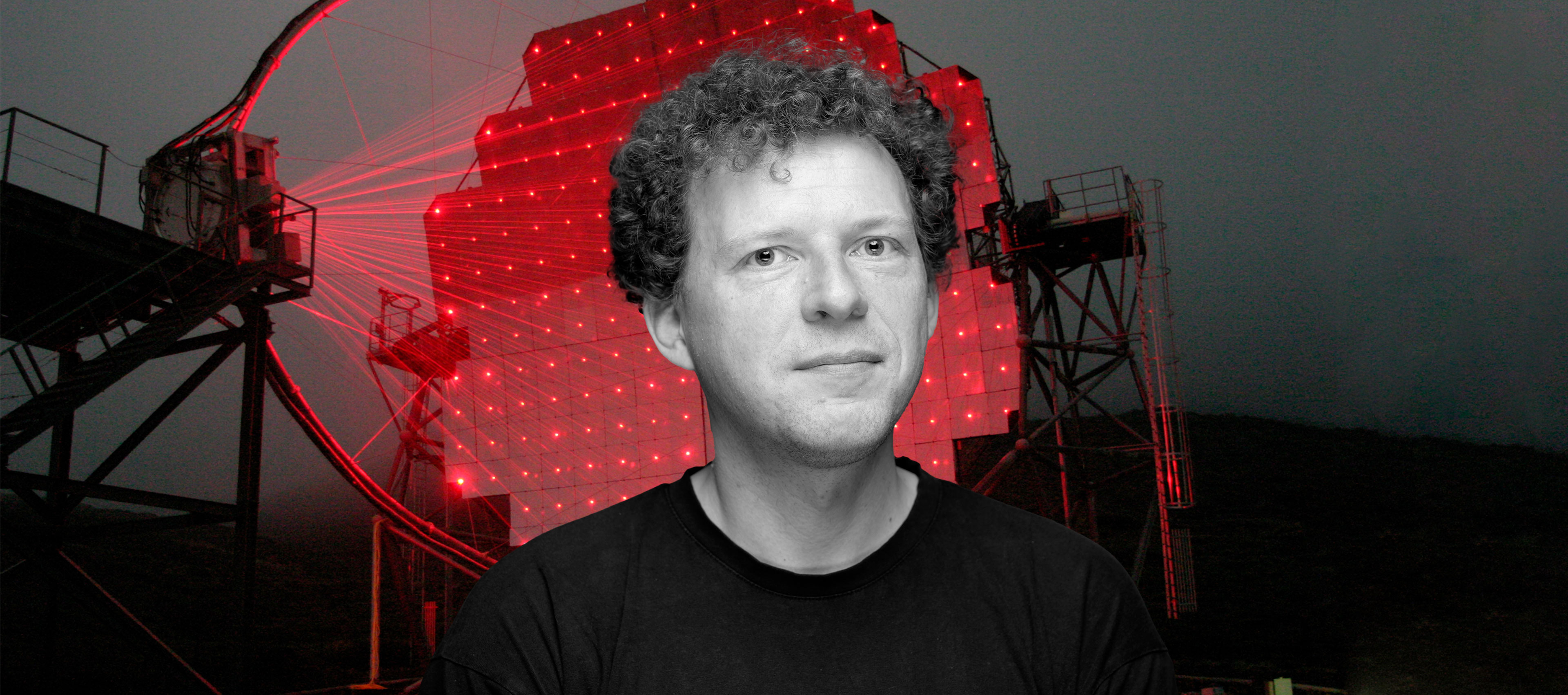 Profesor Julian Sitarek na tle rozświetlonego czerwonymi laserami teleskopu czerenkowskiego