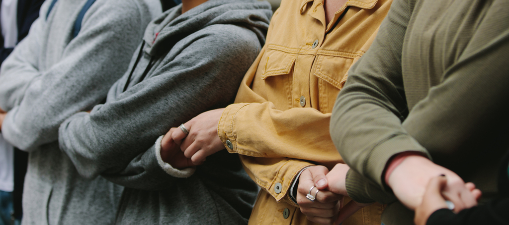 Osoby stojące obok siebie w rzędzie trzymają się za ręce