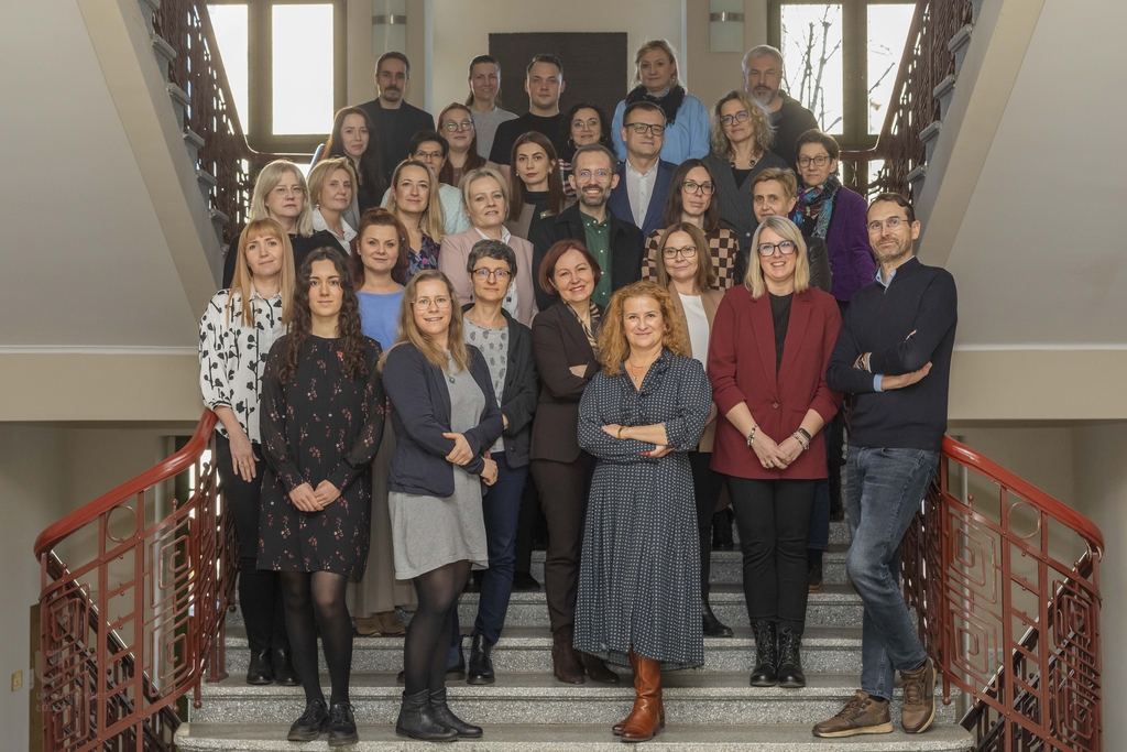 Duża grupa ludzi, kobiet i mężczyzn, stojących na schodach na klatce schodowej Uniwersytetu Łódzkiego.