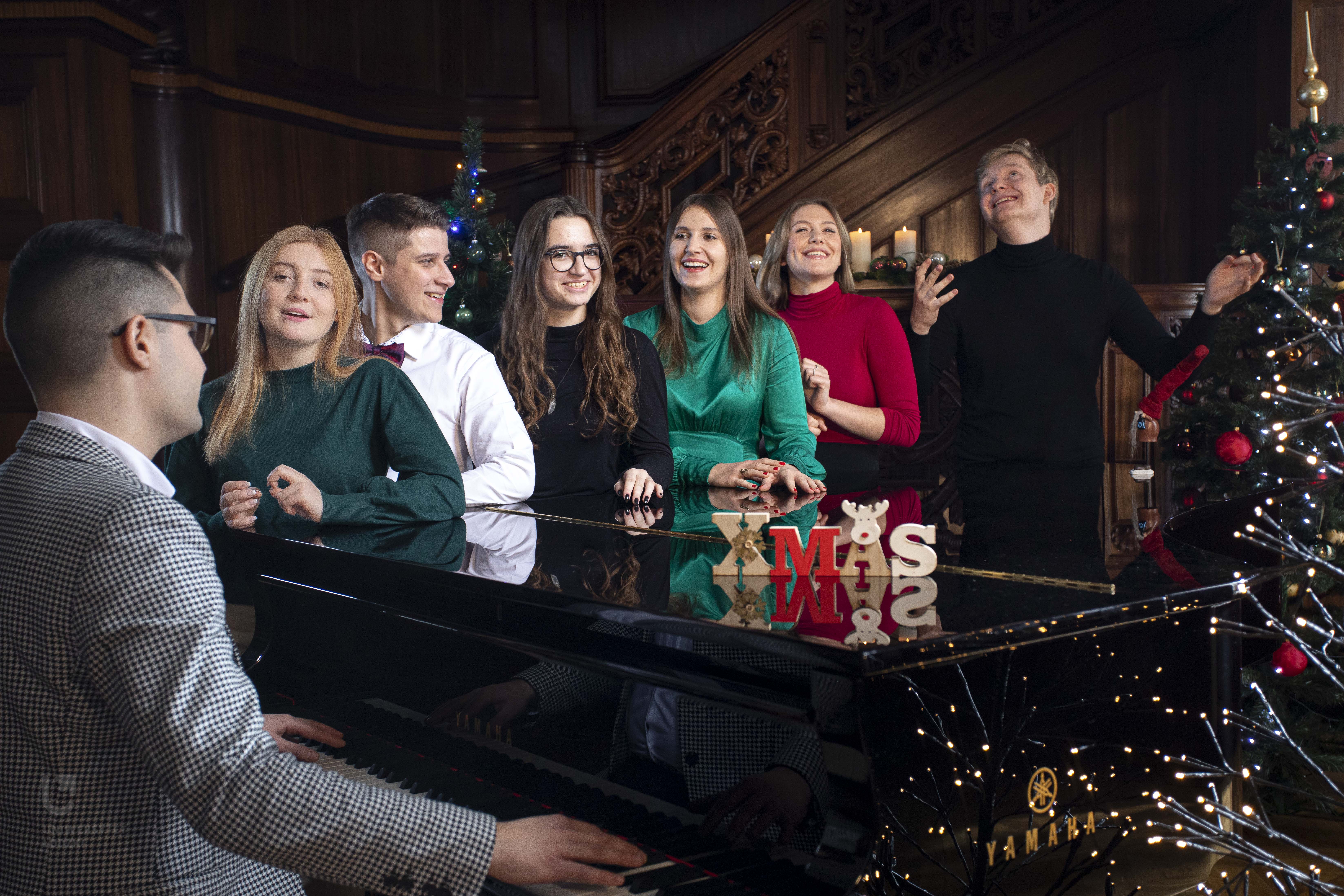 Studenci UŁ w świątecznych strojach stojący przy fortepianie i śpiewający kolędy