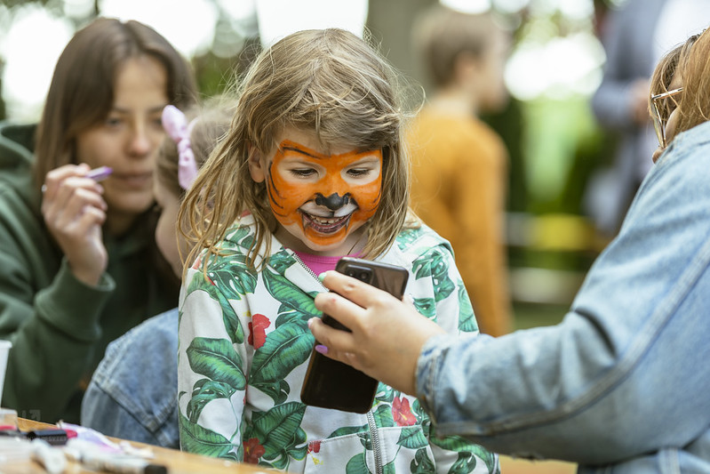 Dziewczynka z malunkiem tygrysa na twarzy , oglądająca zdjęcie na telefonie.