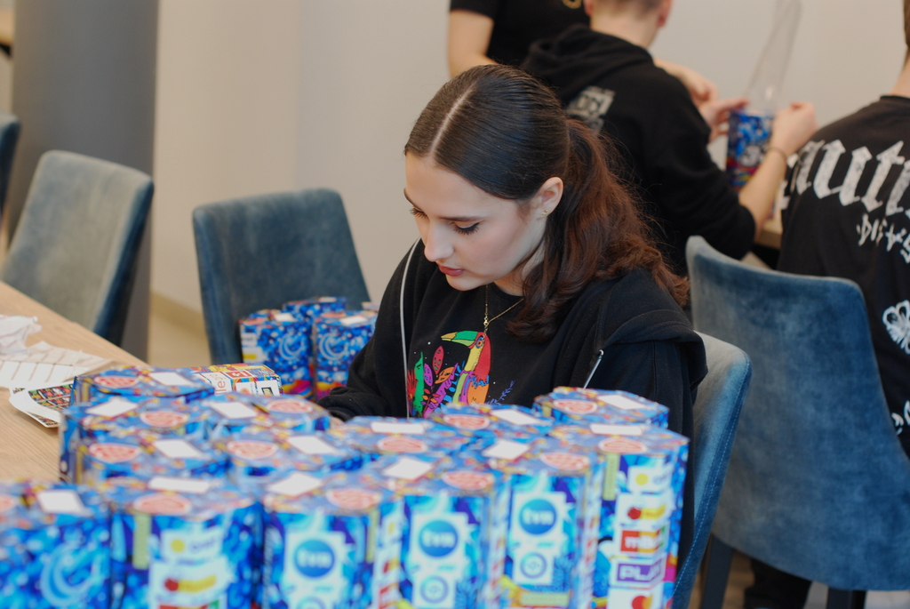 Studentka ze sztabu WOSP UŁ siedząca przy stole z puszkami na zbiórkę WOSP