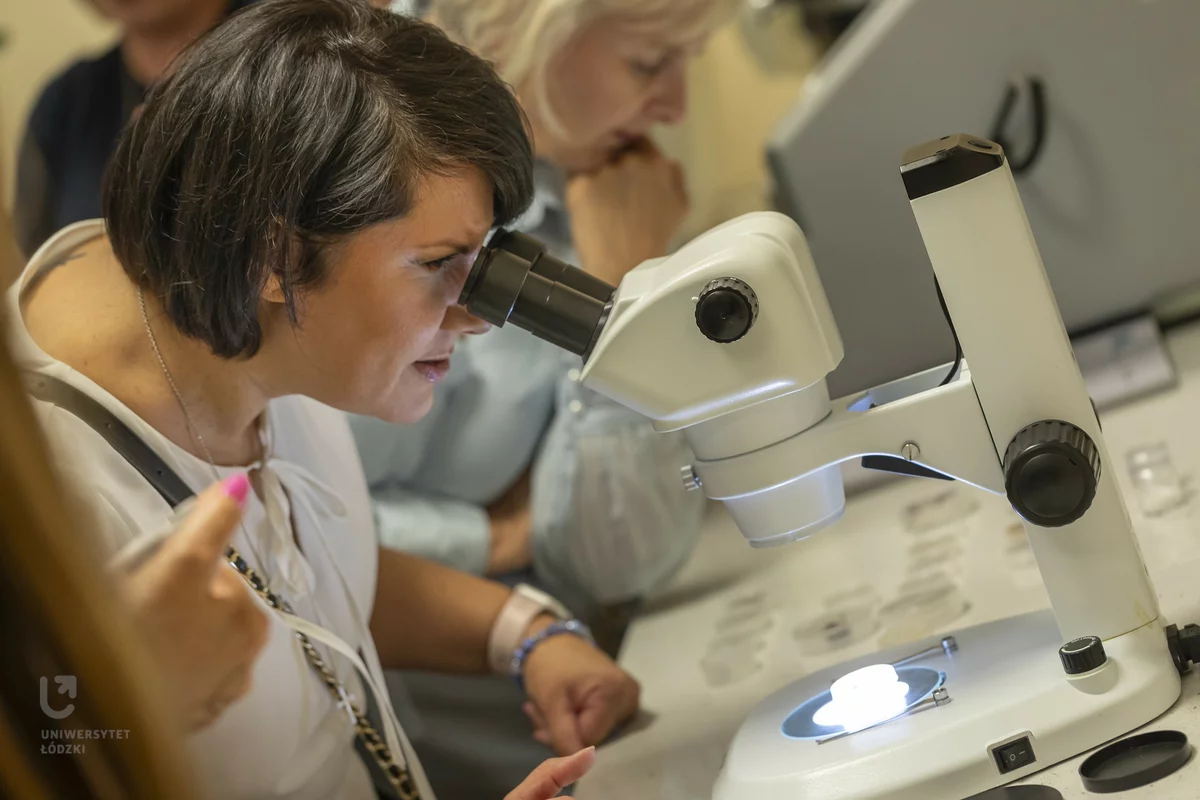 zdjęcie przedstawia kobietę, która patrzy przez okular mikroskopu