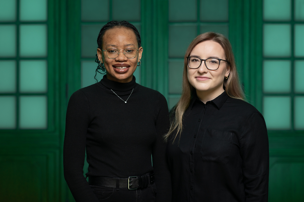 Zdjęcie Julity Maciejewskiej i Rumbidzai Hodzong. Dwie dziewczyny stoją obok siebie, są ubrane na czarno.