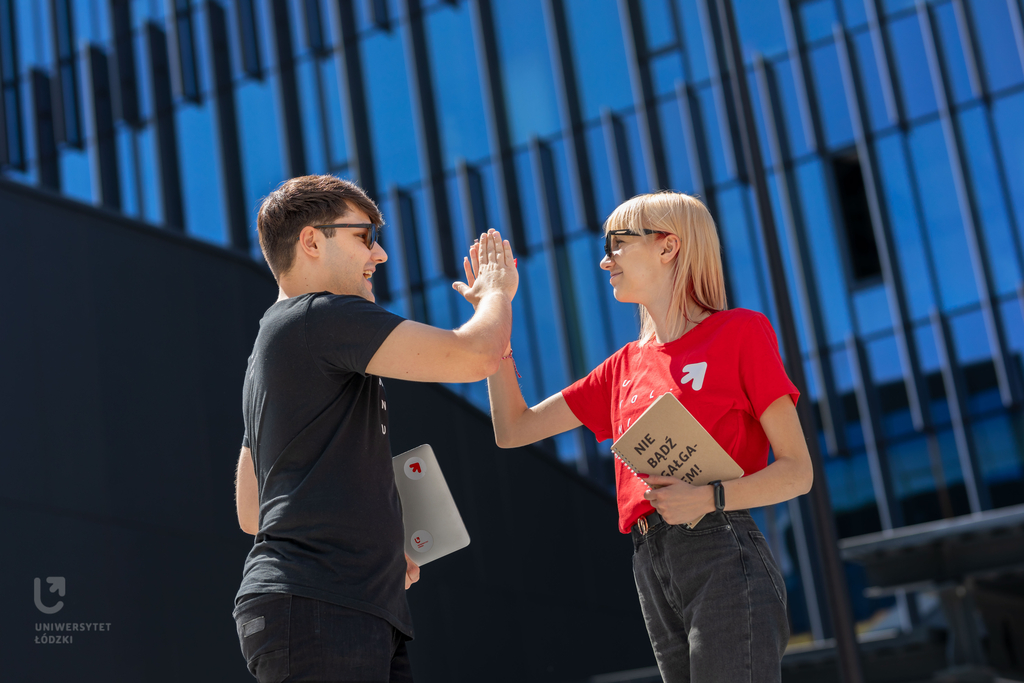 Dwoje młodych ludzi, dziewczyna i chłopak, stoją na dworze w słoneczny dzień i przybijają sobie piątkę