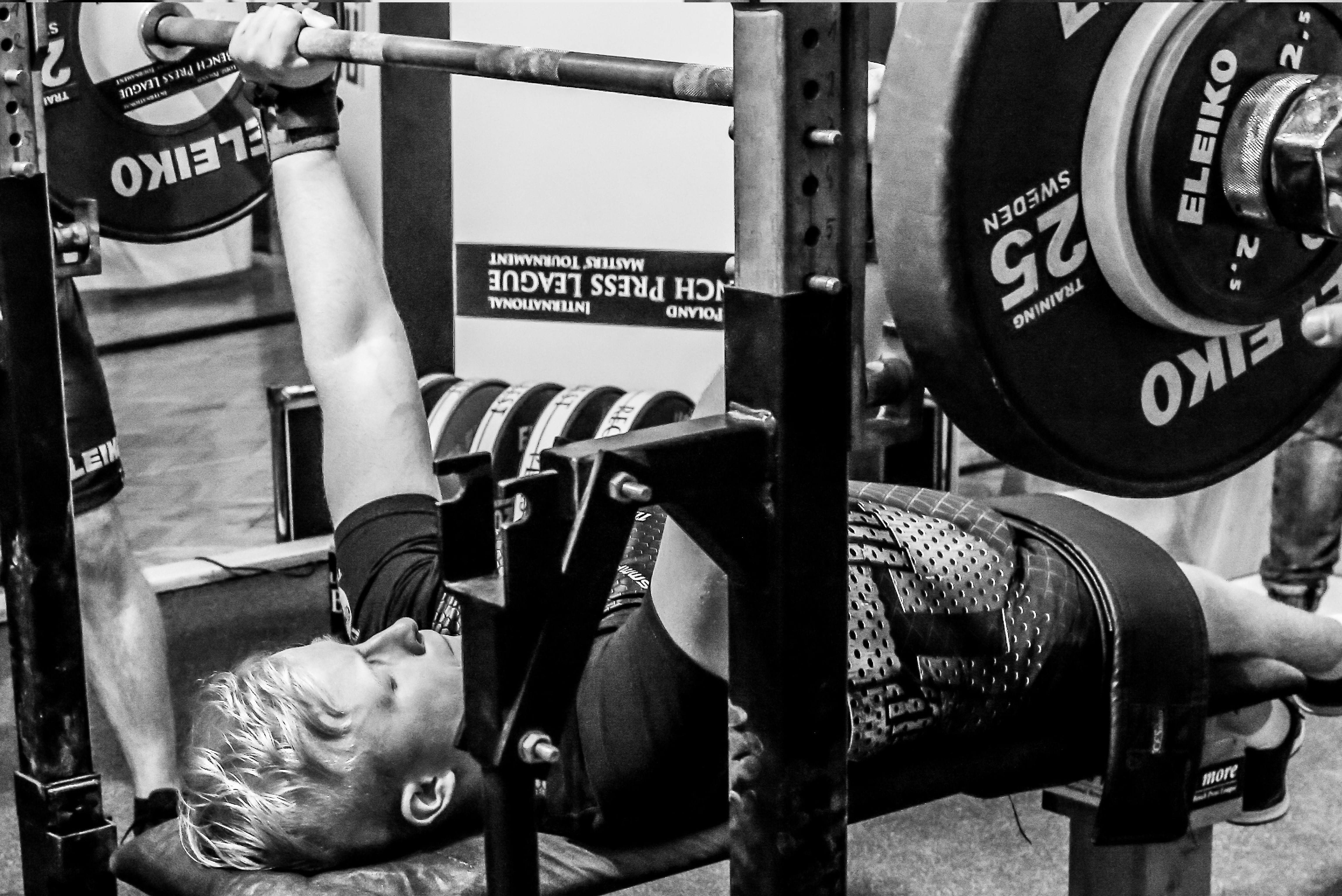 Mężczyzna z niepełnosprawnością podnosi sztangę leżąc